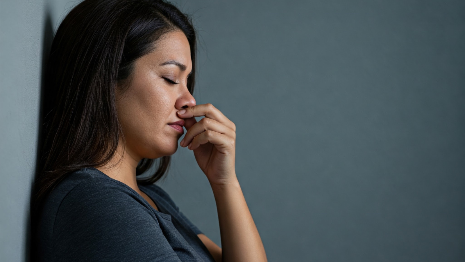Eine Frau lehnt mit geschlossenen Augen an einer Wand – Ausdruck von innerem Druck, Überforderung und emotionaler Erschöpfung.